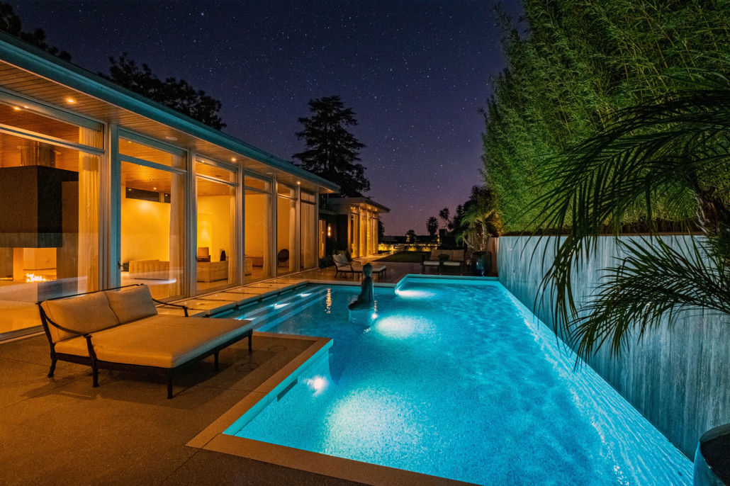 Illuminated pool alongside a modern home with full-height glass doors
