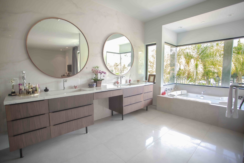 Bright bathroom with a double vanity, circular mirrors and a bath beside the window